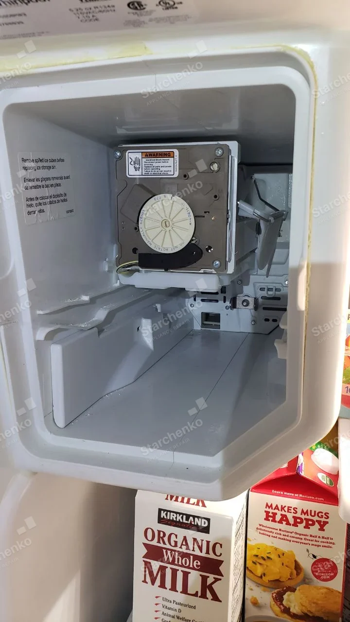 Open Whirlpool freezer ice-maker area with collection bin removed and ice-maker mechanism exposed.