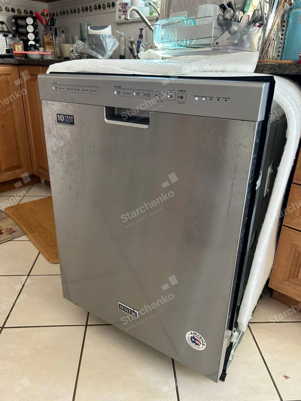 Maytag nameplate near bottom of stainless dishwasher door, unit pulled out with side insulation visible.