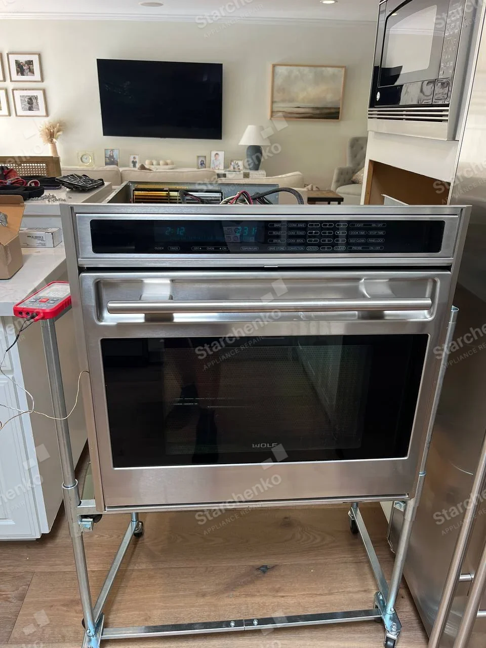 Built-in Wolf wall oven pulled out onto wheeled stand, top cover off showing blower and wiring.