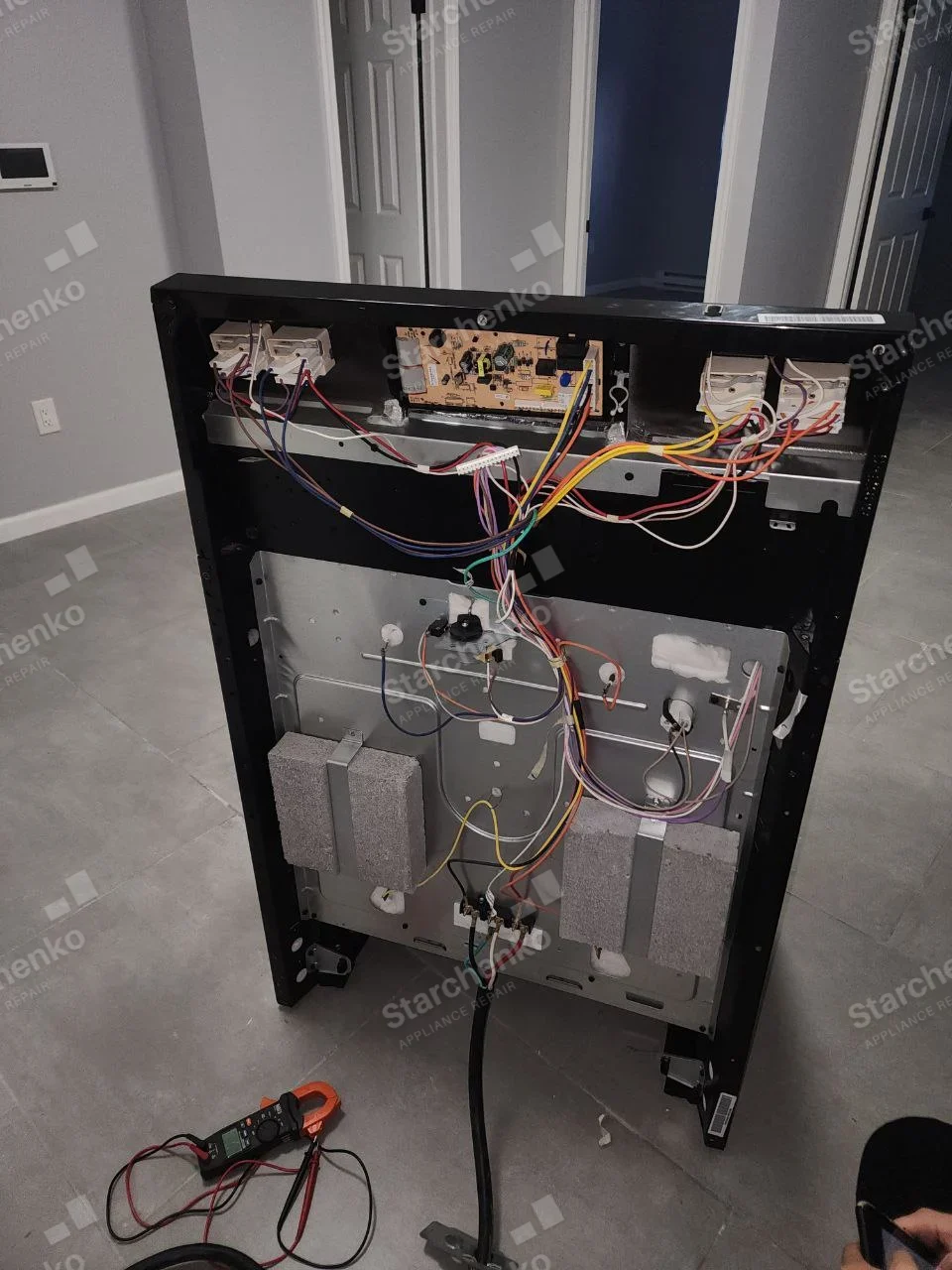 Kenmore repair: Rear of cooking range pulled out, upper control board exposed and rear of insulated oven cavity, electric power cable.