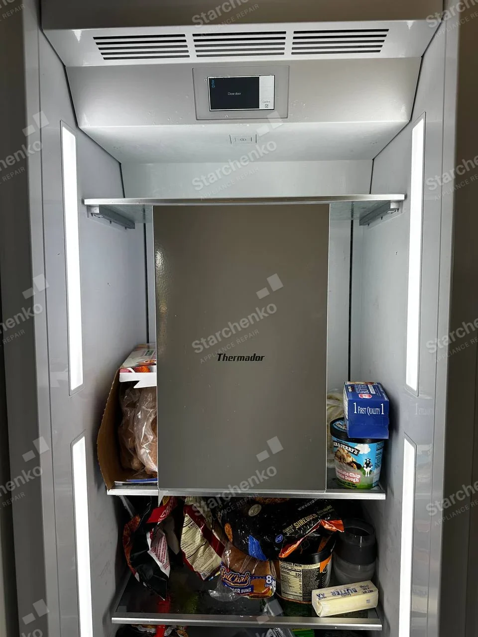 Thermador repair: Refrigerator interior with lit side walls and service panel placed on shelf, digital display says close door.