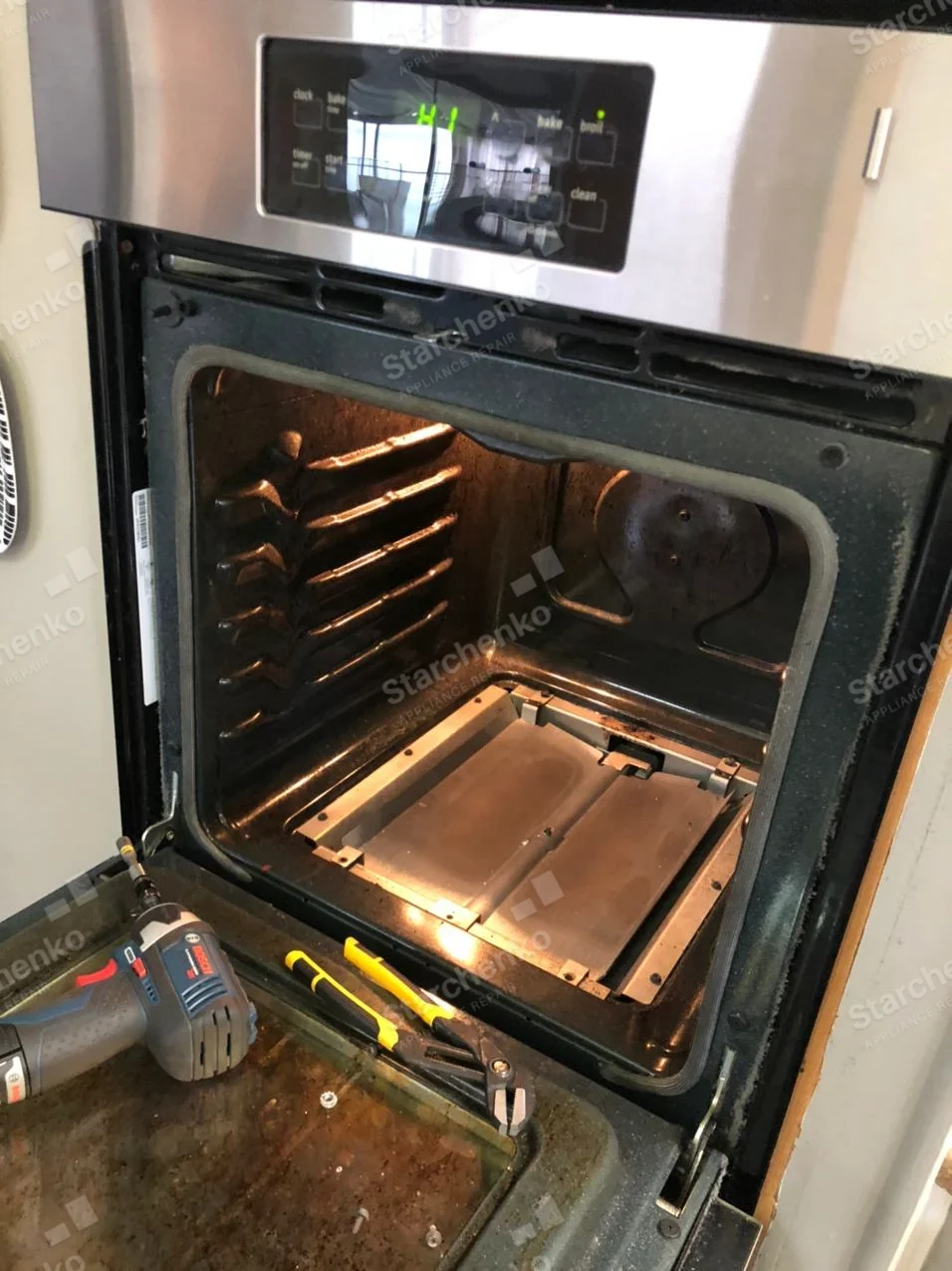 Electrolux repair: Open wall oven with bottom cavity panel removed and tools resting on open door.