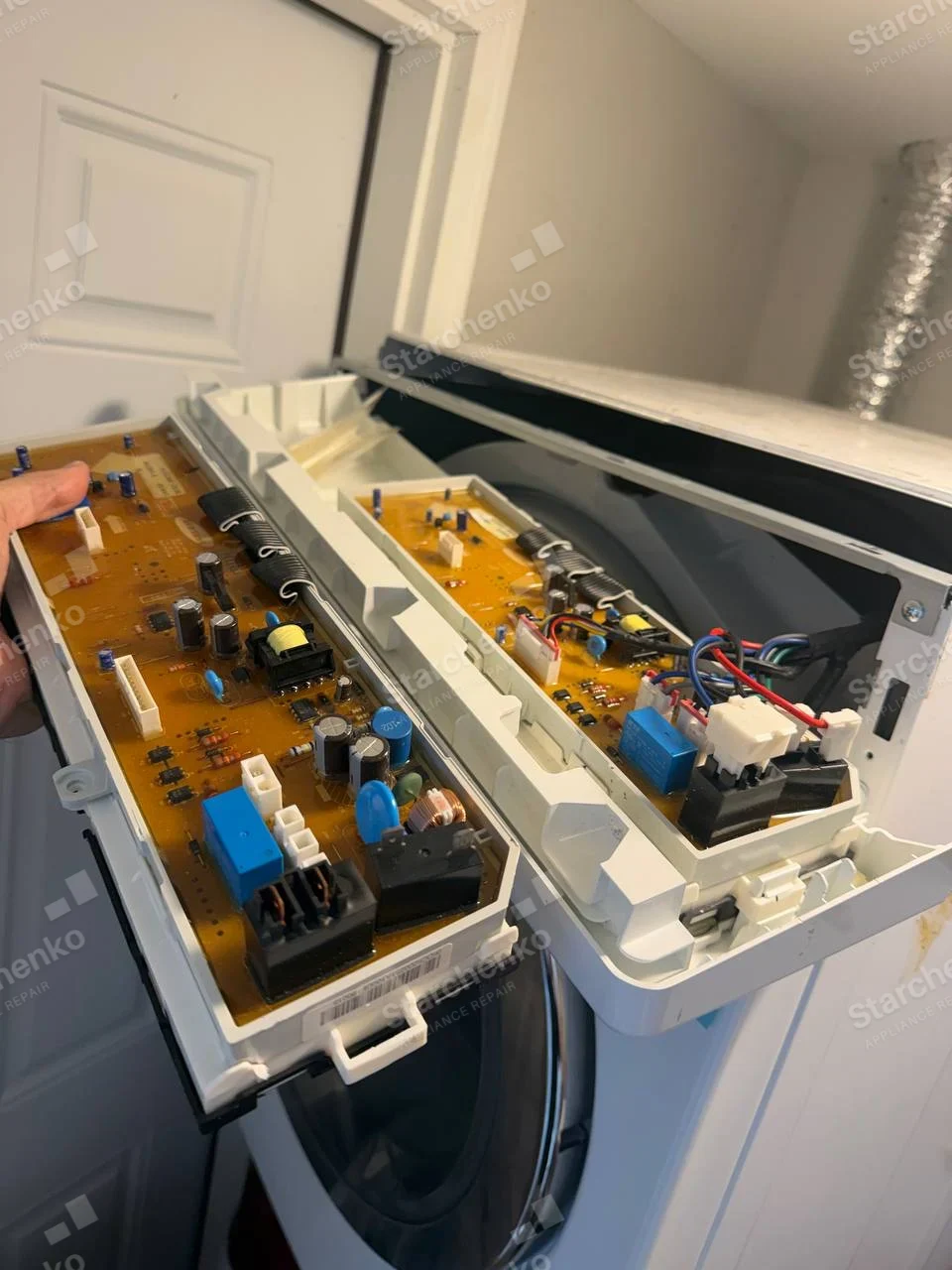 Frigidaire repair: Open laundry control console with circuit boards, round door, and dryer exhaust duct behind.