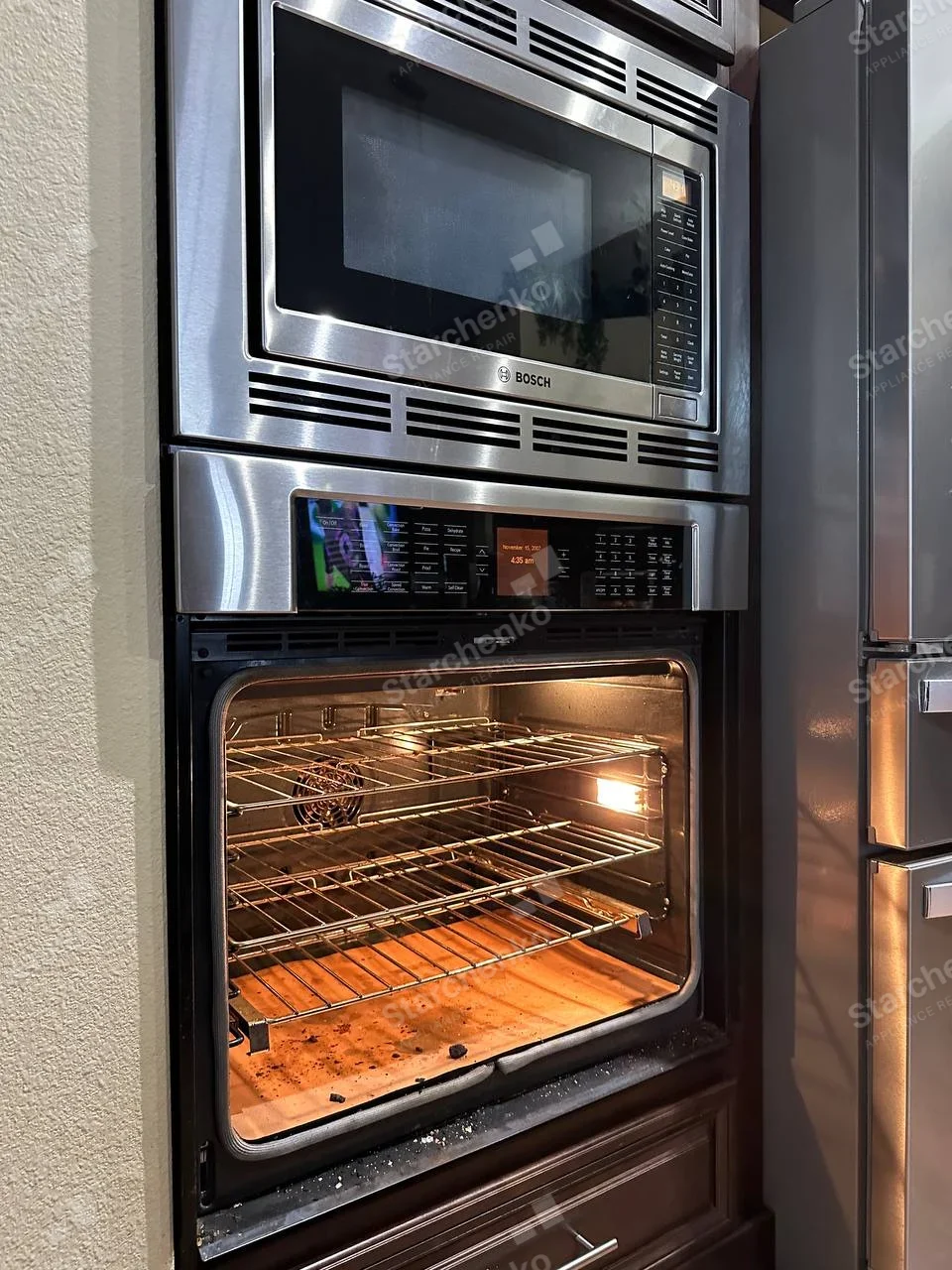 Electrolux repair: Lower wall oven cavity open and lit with removed door, Bosch badge visible only on separate microwave above.