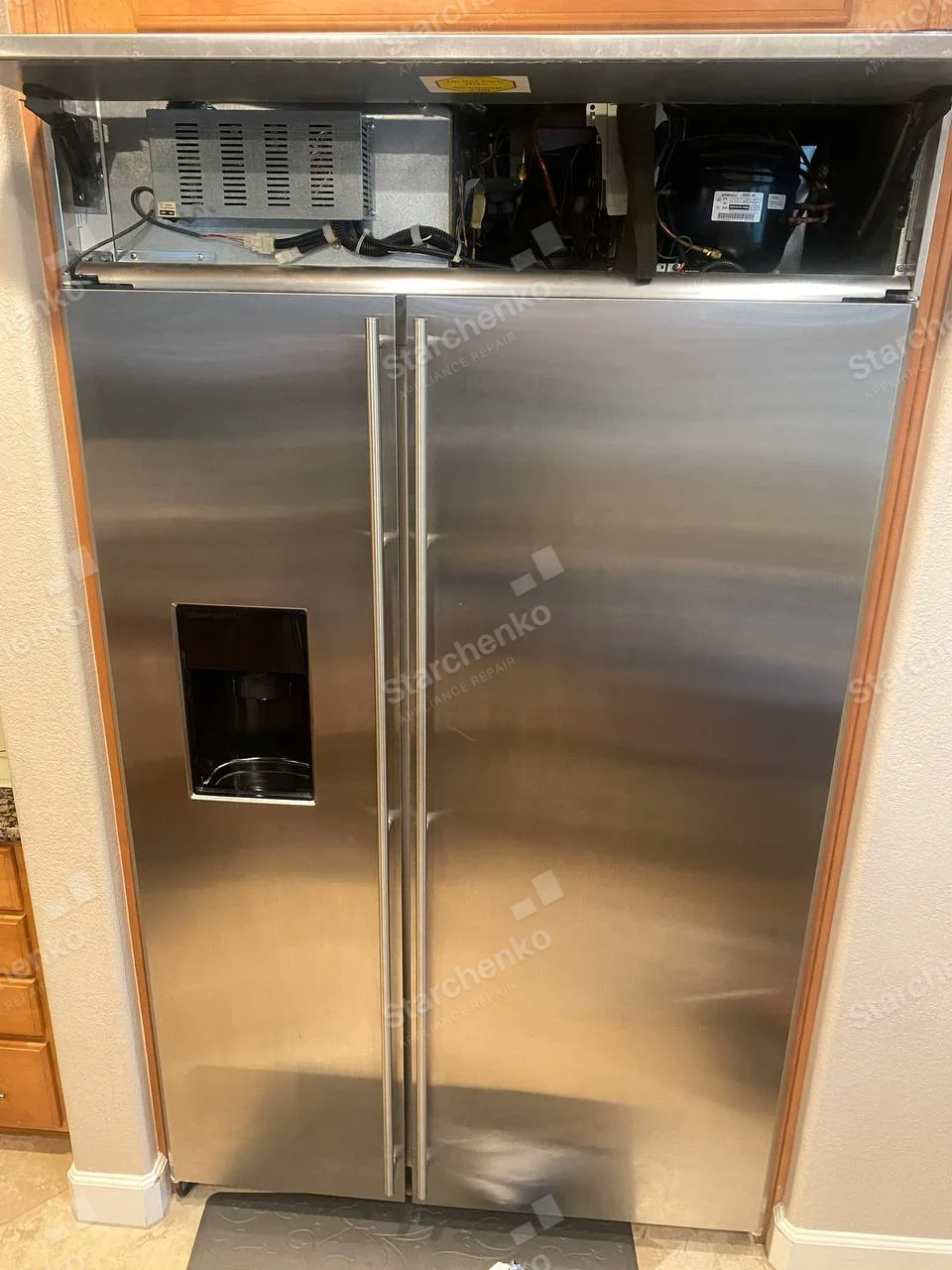 Viking repair: Large built-in stainless side-by-side refrigerator with ice dispenser, upper service grille removed, exposing compressor and electronics.