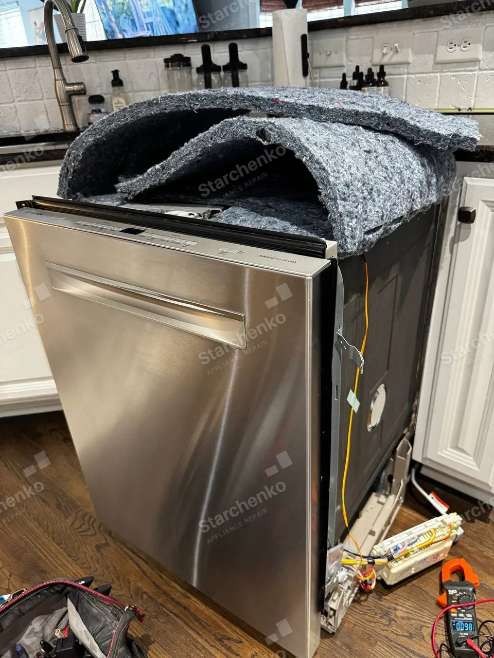 LG repair: Stainless dishwasher pulled from kitchen cabinet with sound blanket lifted and electrical modules exposed at side, no maker badge.