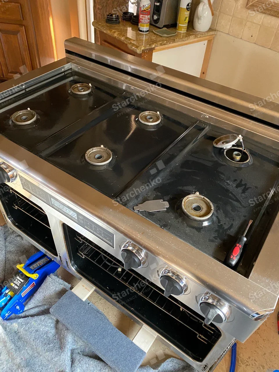 Dacor repair: Wide dual-oven gas range with burner caps and grates removed, open oven cavities and tools nearby.