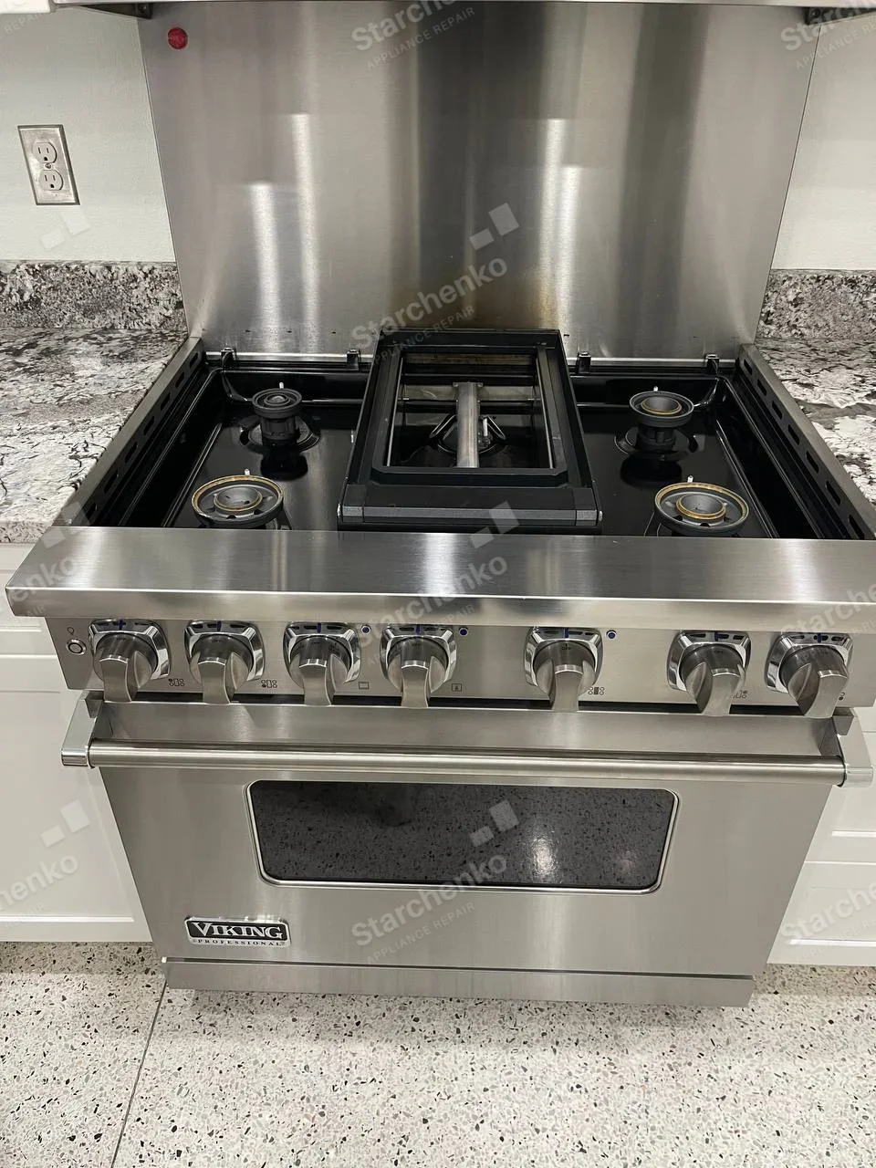 Viking repair: Wide gas range with burner caps lifted and central griddle assembly exposed over oven.