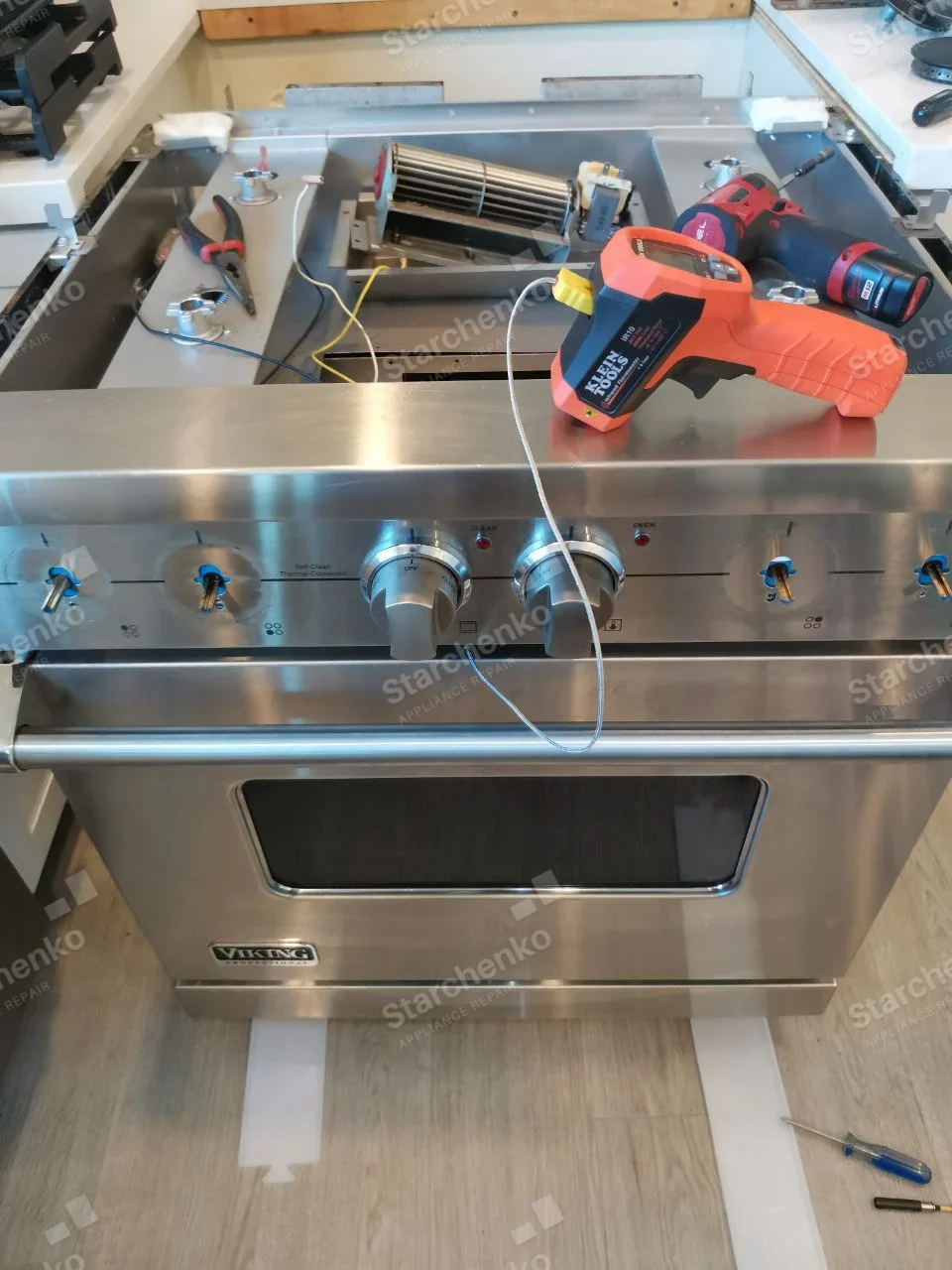 Viking stainless range with cooktop and several knobs removed, exposing internal blower.