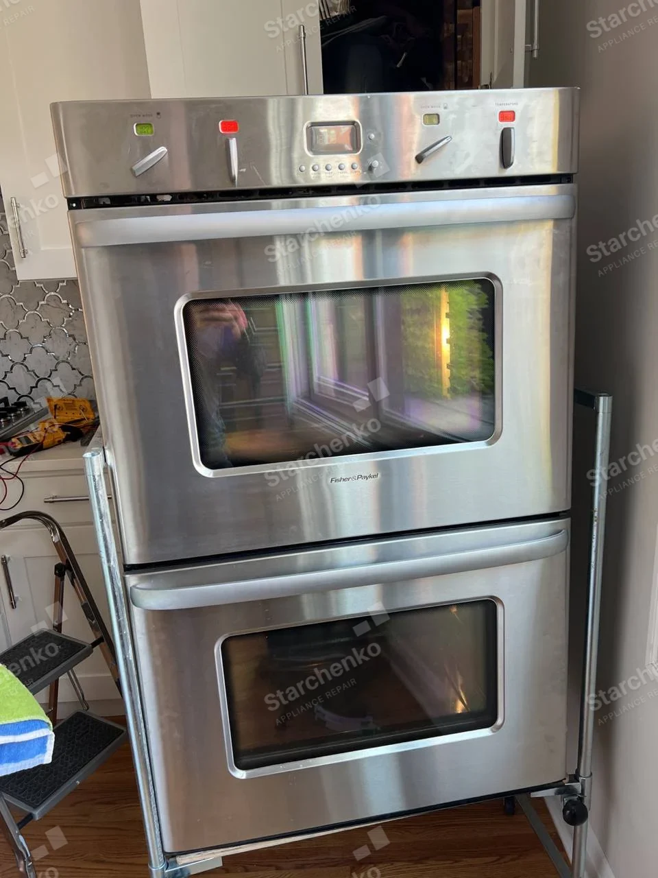 Stainless Fisher & Paykel double wall oven pulled out from cabinetry on rolling stand.