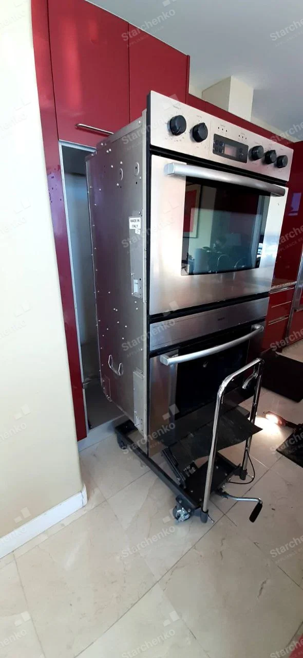 Electrolux repair: Stainless stacked oven and microwave unit pulled from red cabinetry on wheeled lift.