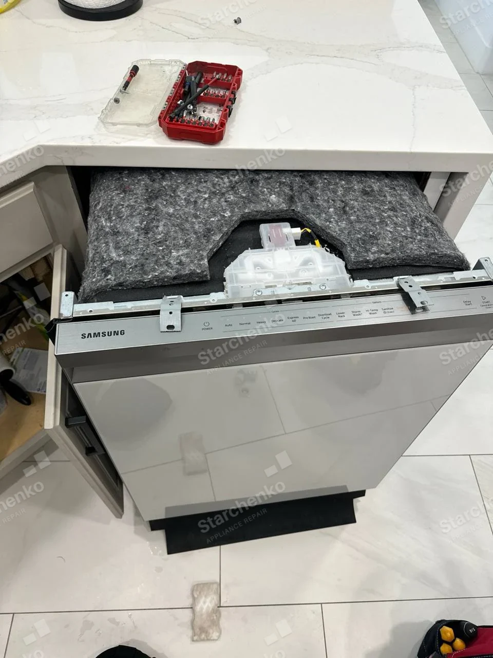 SAMSUNG name on dishwasher top control strip, unit pulled from cabinet with top insulation and control module exposed.