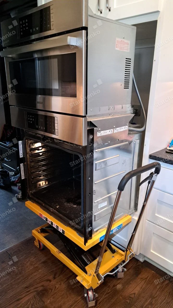 Electrolux repair: Lower wall oven pulled out on lift, oven door removed and cavity lit, Bosch wordmark clearly on the separate microwave above.