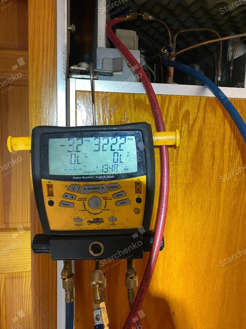 Thermador repair: Refrigeration service hoses and digital manifold connected to upper service bay in wood-paneled built-in cabinet.