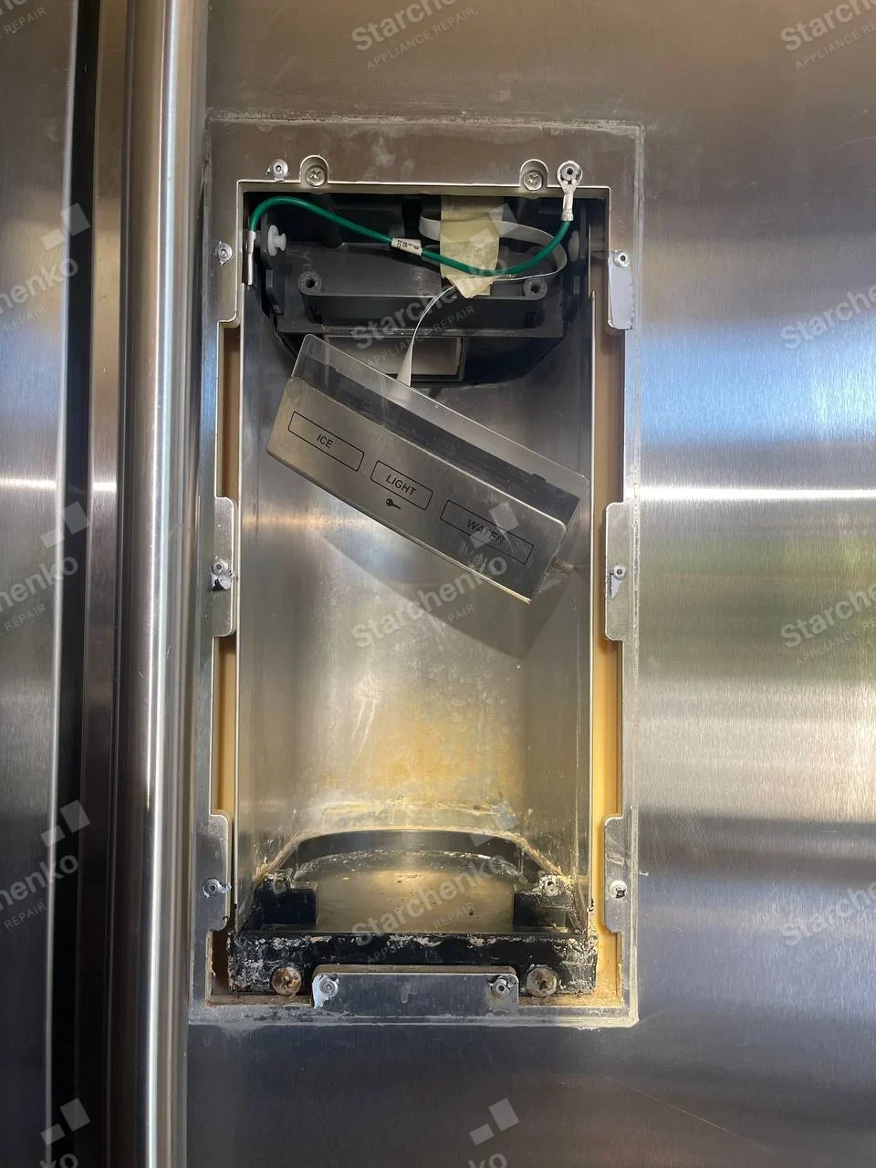 KitchenAid repair: Refrigerator door water and ice dispenser assembly exposed with ICE LIGHT WATER control hanging loose.