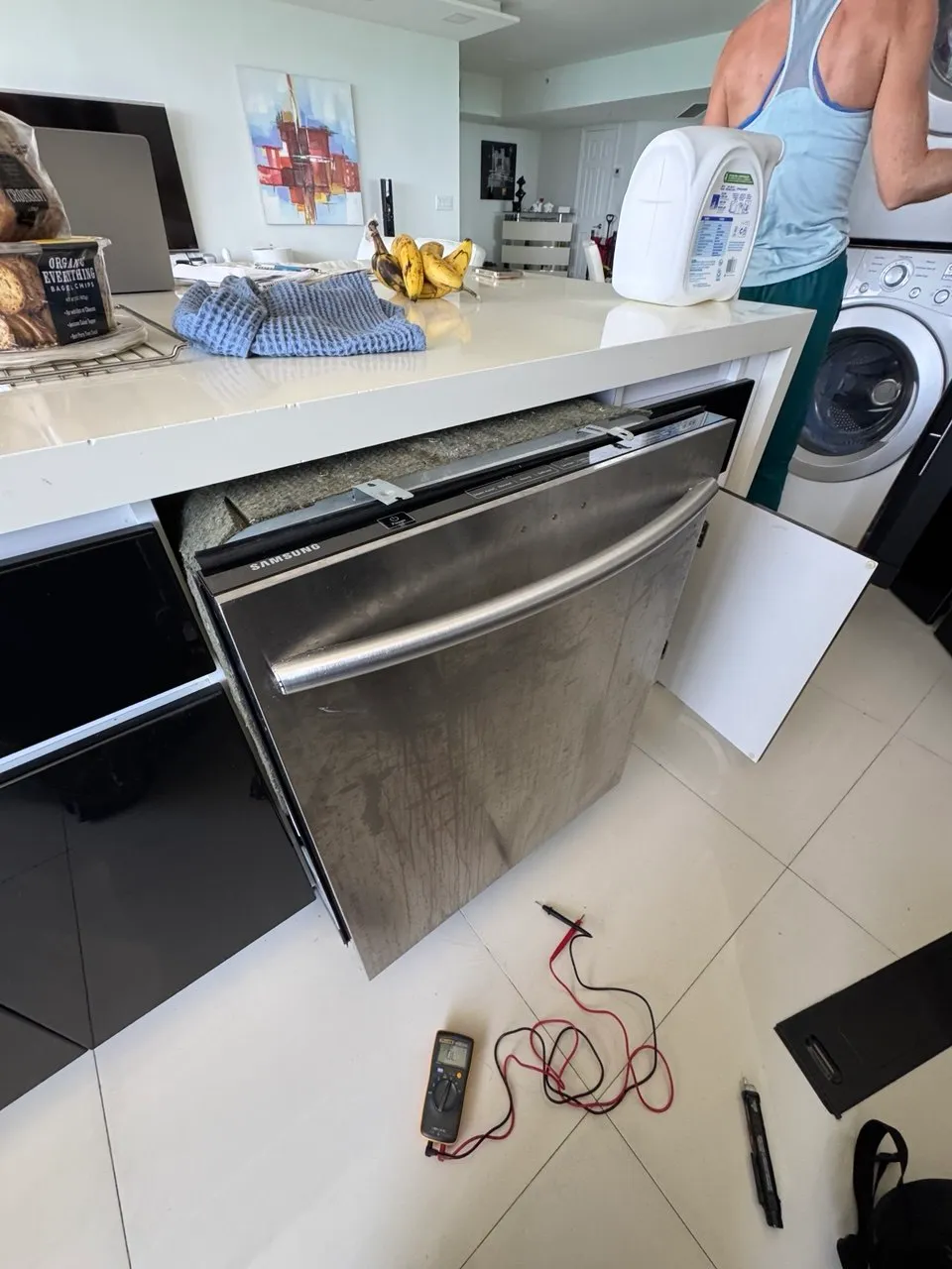 Stainless dishwasher pulled out from under the counter with a multimeter on the floor