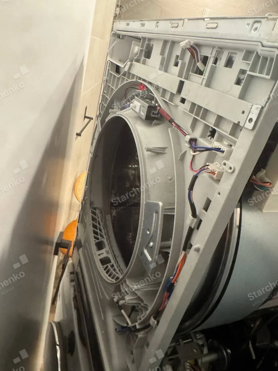 Samsung front-load dryer housing disassembled, exposing drum opening and door-switch wiring.