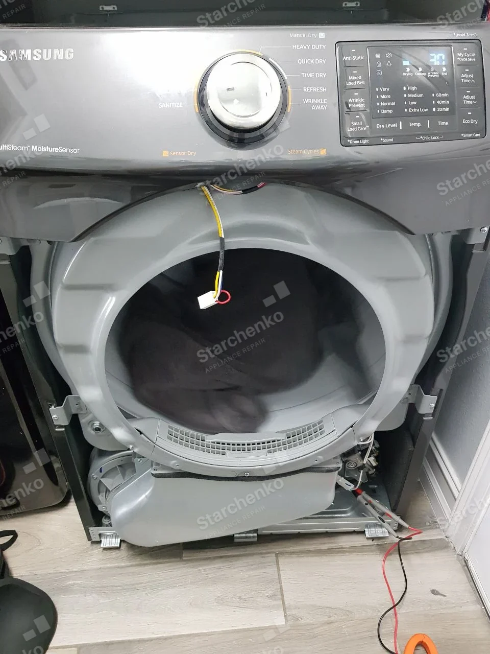 Samsung dryer front opened with drum housing, blower assembly and wires exposed.
