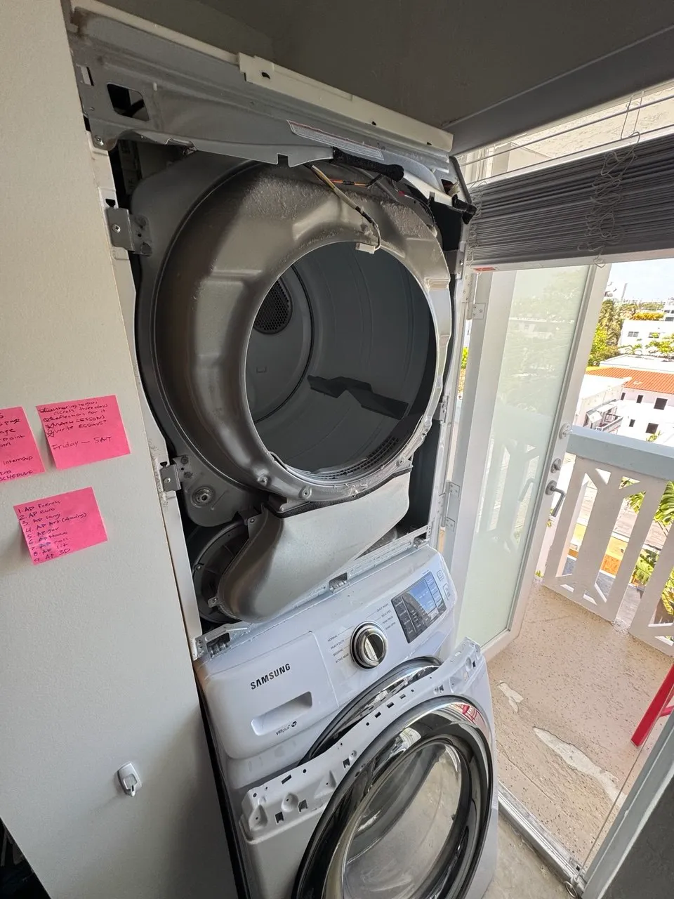 Stacked washer-dryer opened in a condo balcony laundry closet with the dryer drum exposed