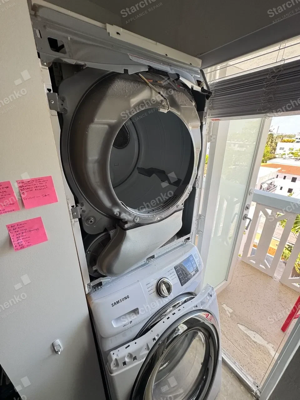 Stacked Samsung washer-dryer opened in a condo balcony laundry closet with the dryer drum exposed