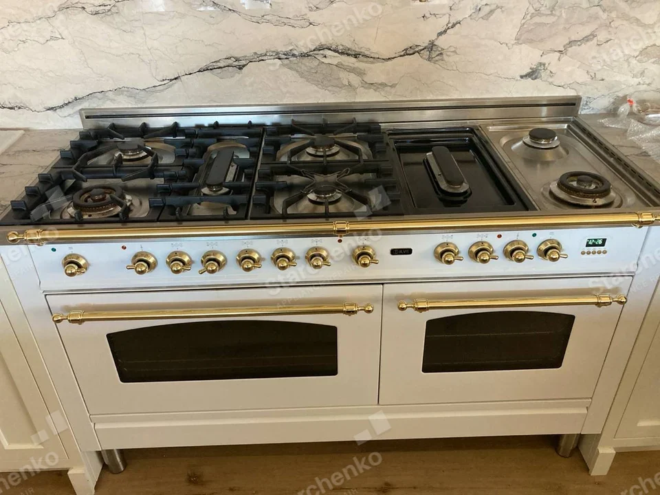 ILVE badge on front center of wide white-and-gold range with twin ovens and gas cooktop.