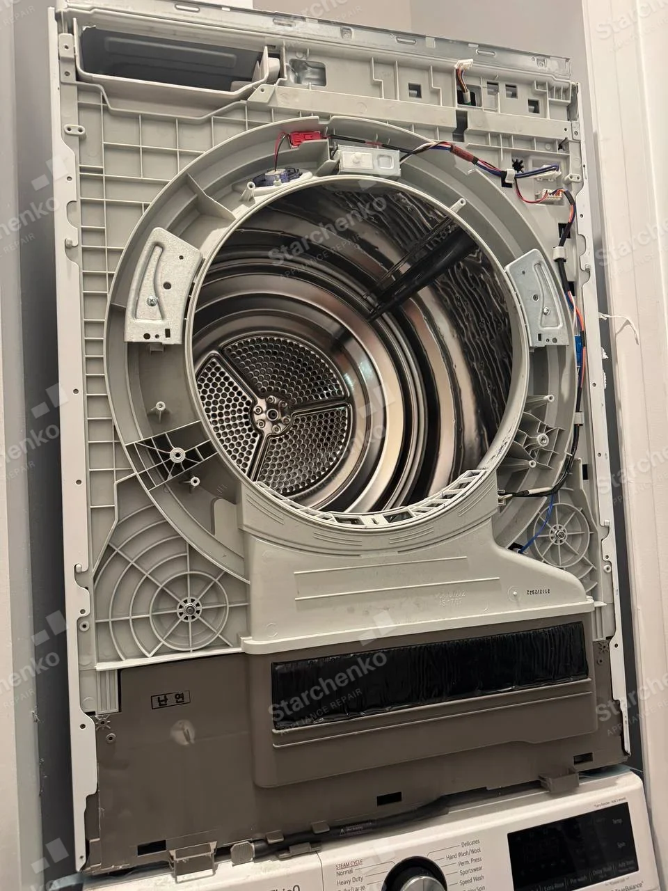 Upper Samsung dryer of laundry stack with front panel removed, drum and lint duct exposed, lower washer controls visible.