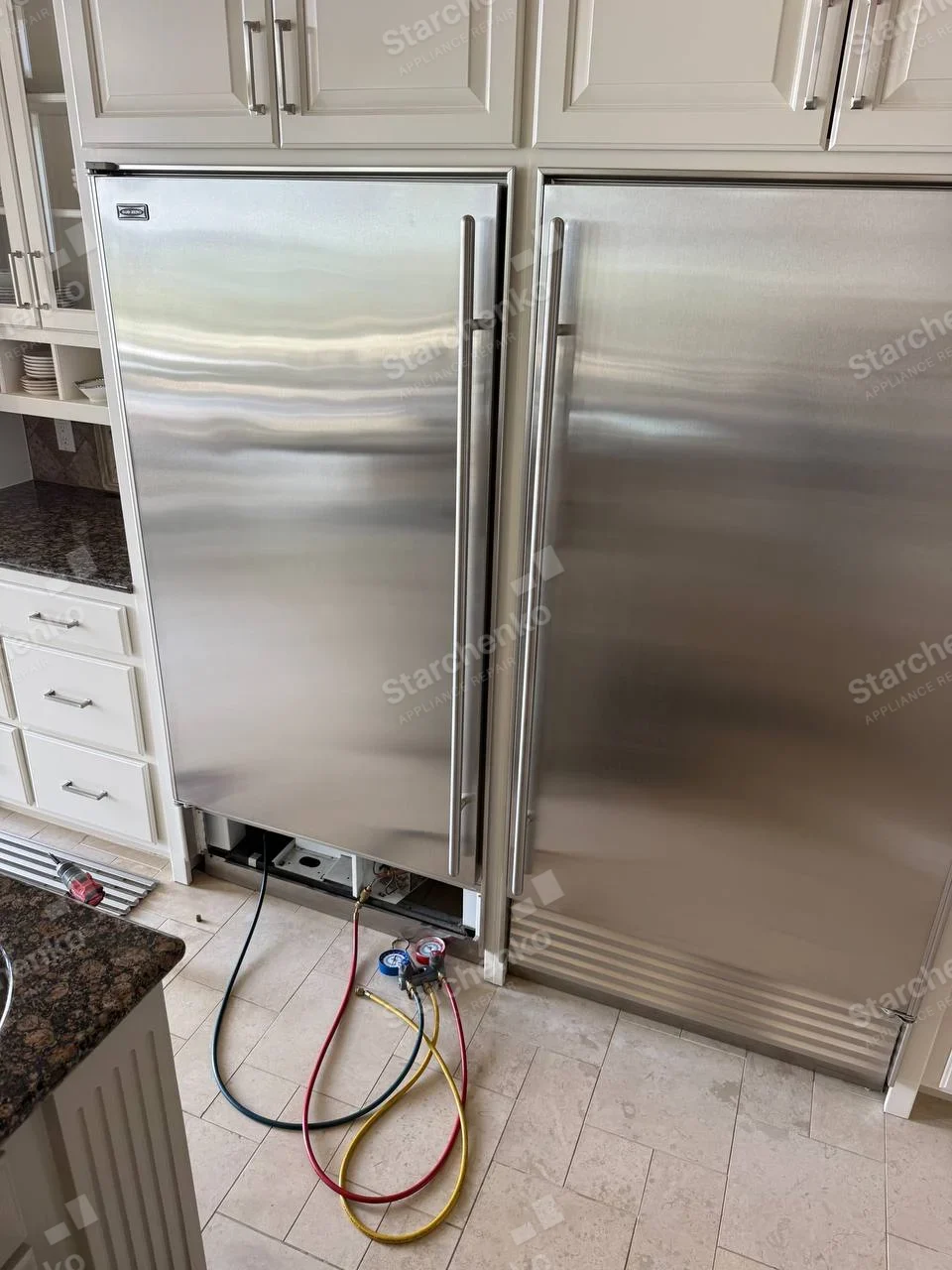 Thermador repair: Service gauges connect at the exposed lower base of the left integrated refrigerator, right-hand matching unit is a neighbour, and small badge on left door is unreadable.