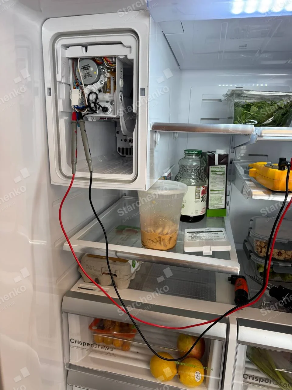 KitchenAid repair: Refrigerator fresh-food compartment ice-maker cover removed, motor and circuit tested with meter, no main-appliance brand visible.