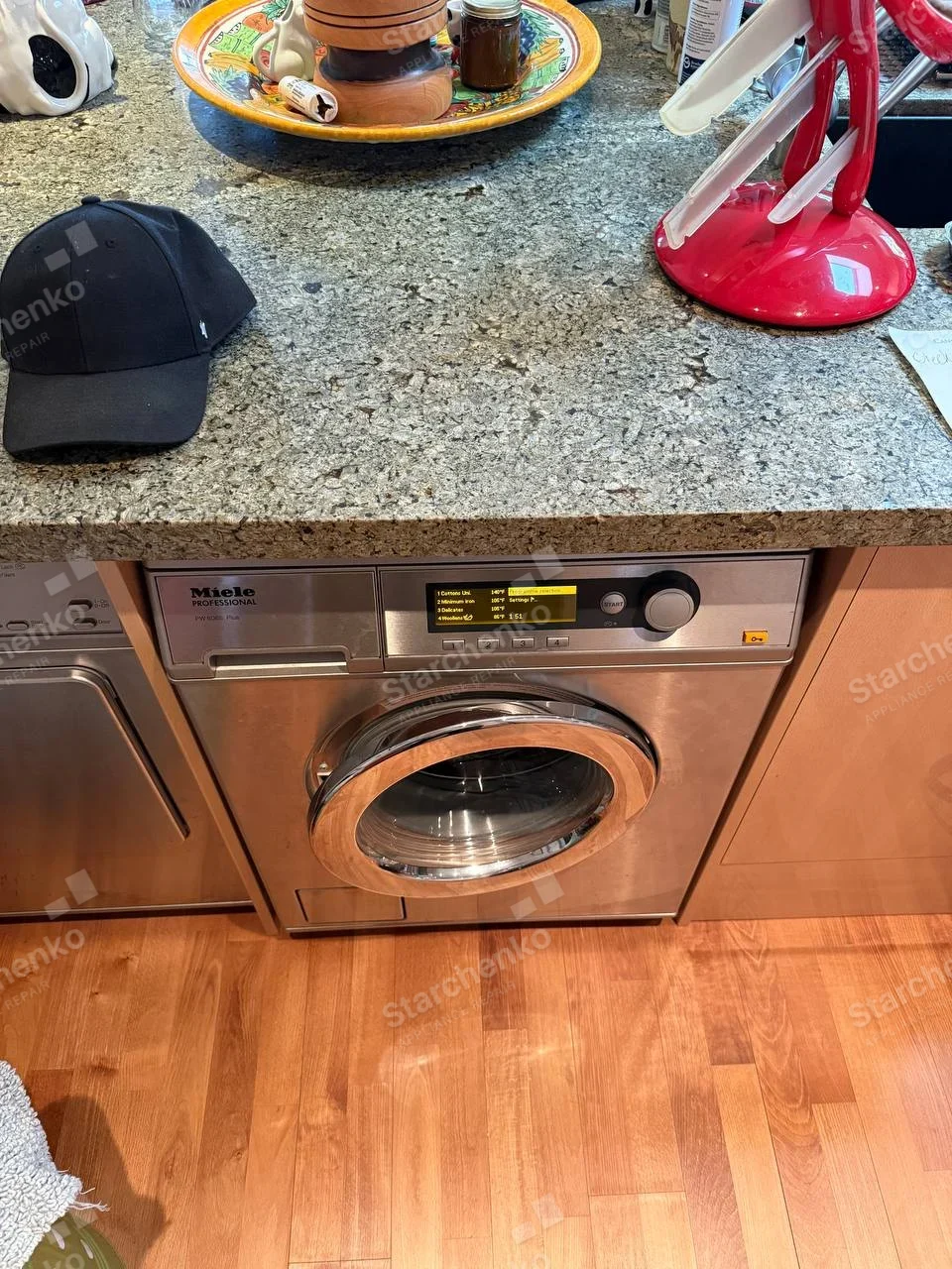 Miele Professional on front control fascia of undercounter front-load washer, neighboring appliance is separate.