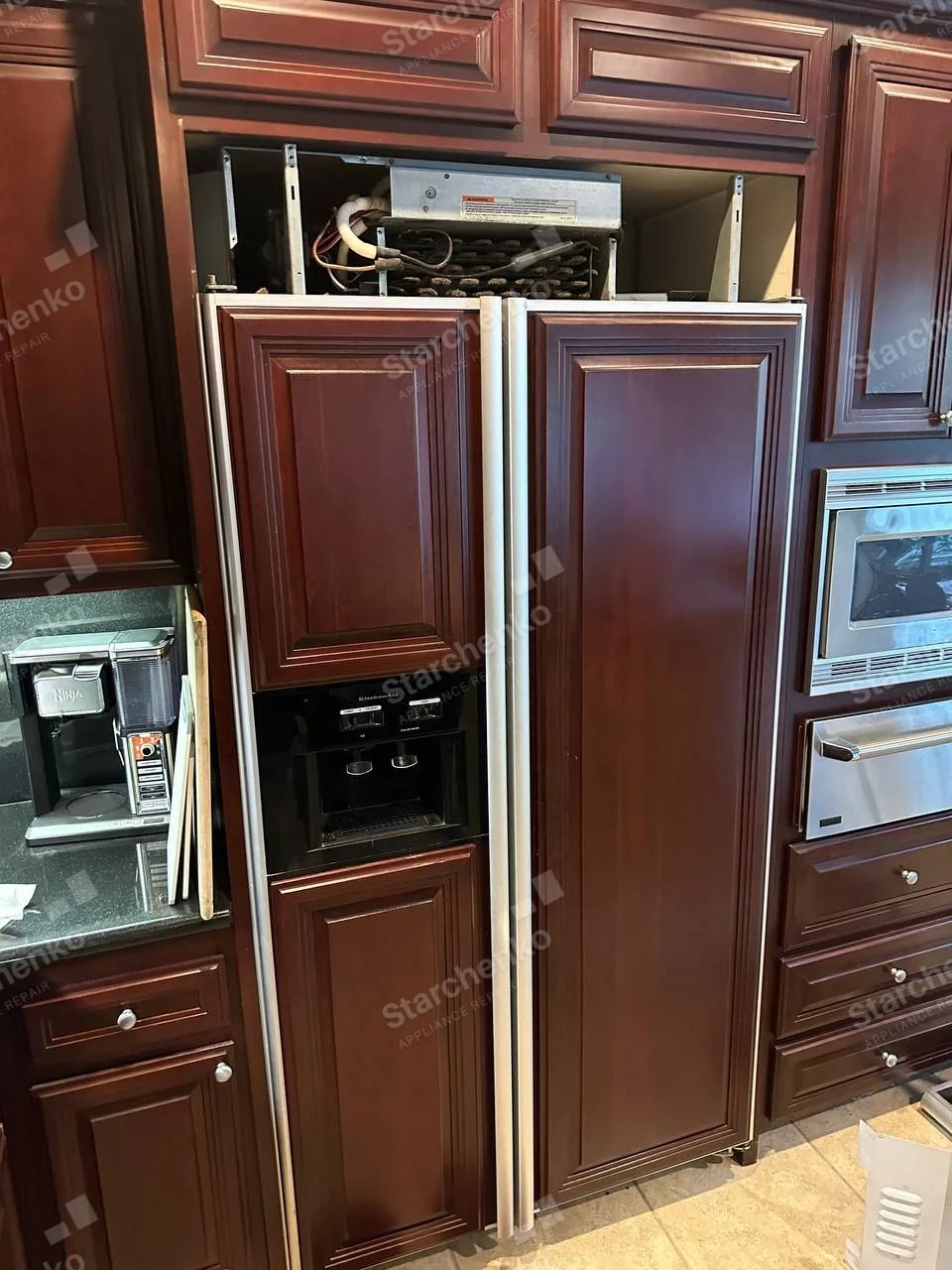 Panel-ready KitchenAid side-by-side refrigerator with top service grille removed and condenser visible.