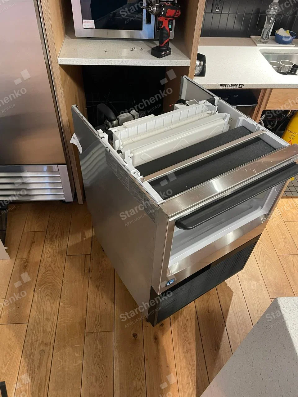 Kold-Draft repair: Compact stainless ice-making unit pulled from under counter, upper ice-making mechanism exposed, small blue oval logo too small to read.