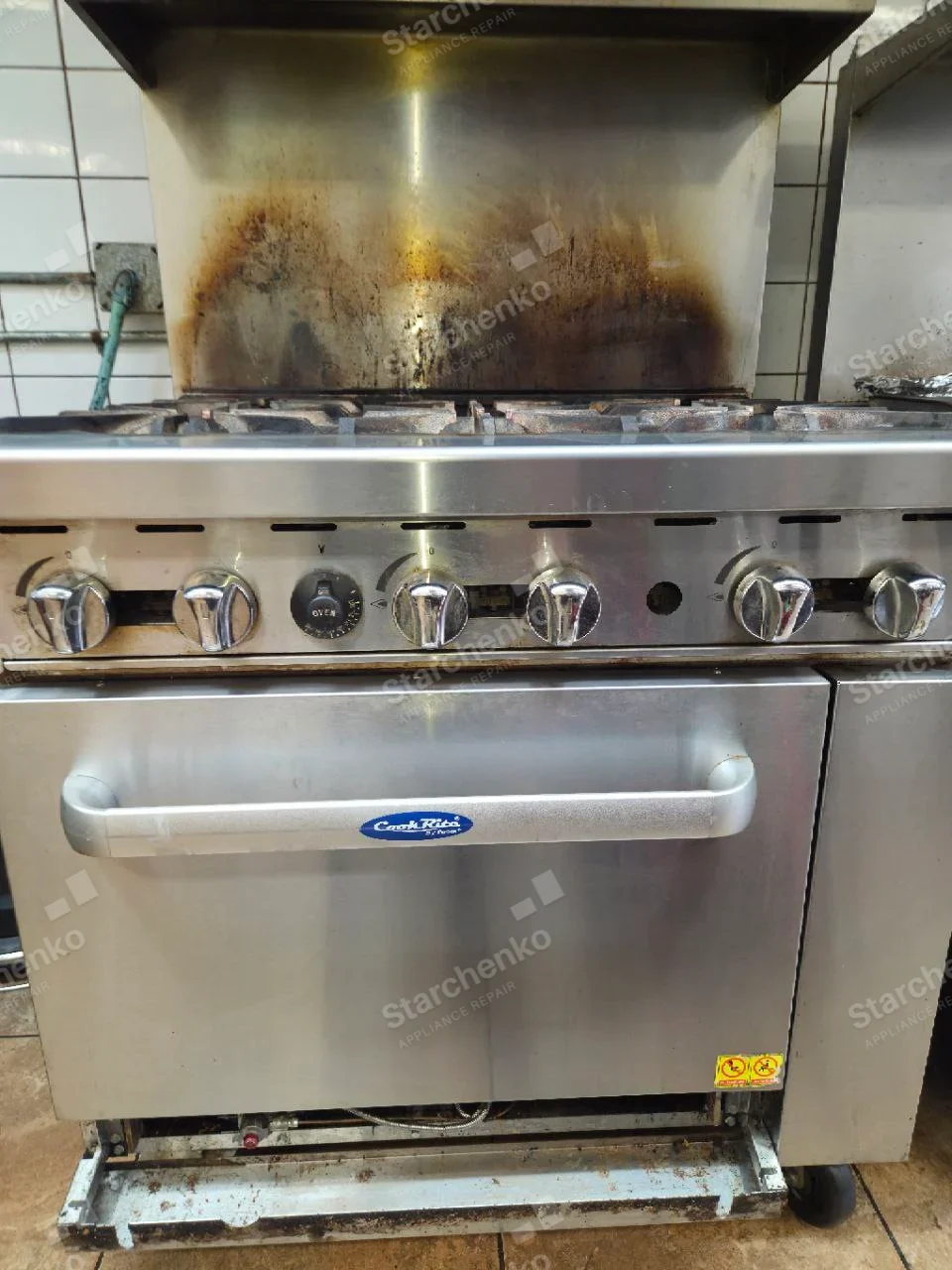 CookRite logo on oven handle of main commercial gas range, front lower trim removed.