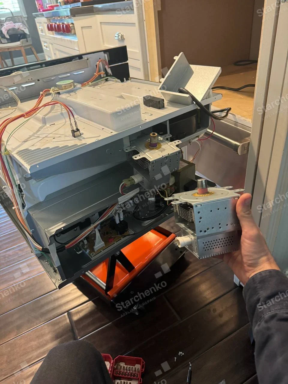 Samsung repair: Dismantled built-in microwave on lift with internal magnetron housing exposed and removed component held nearby.