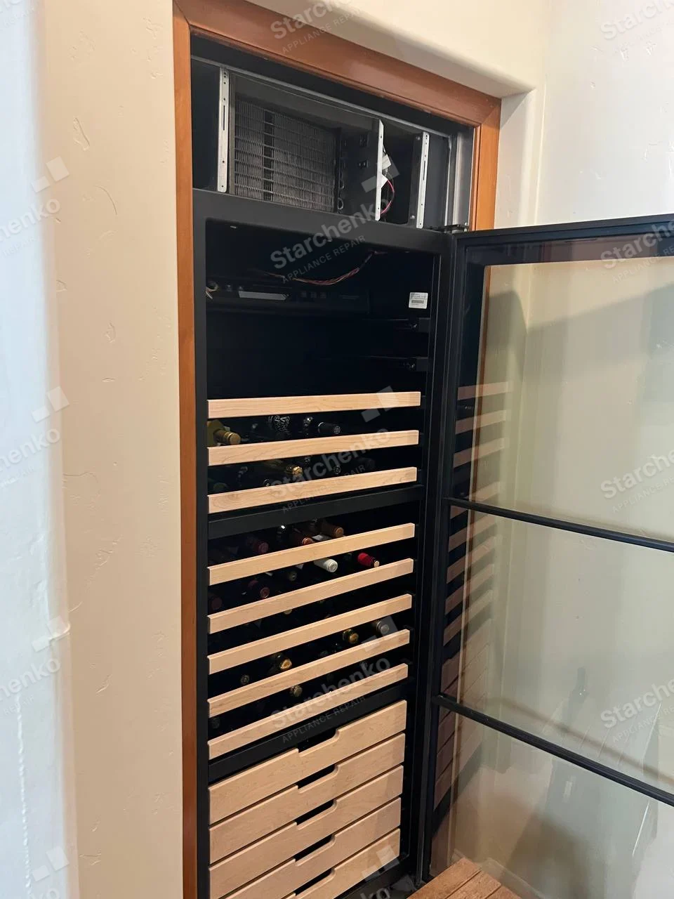 Summit repair: Open glass-door wine cooler with wooden bottle racks and top cooling coil exposed.