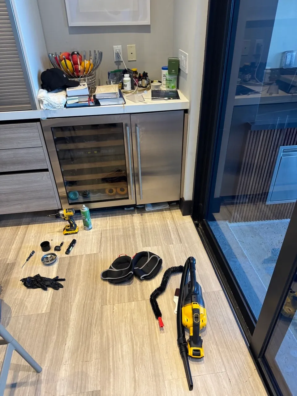 Built-in wine cooler open in a home bar with service tools on the floor