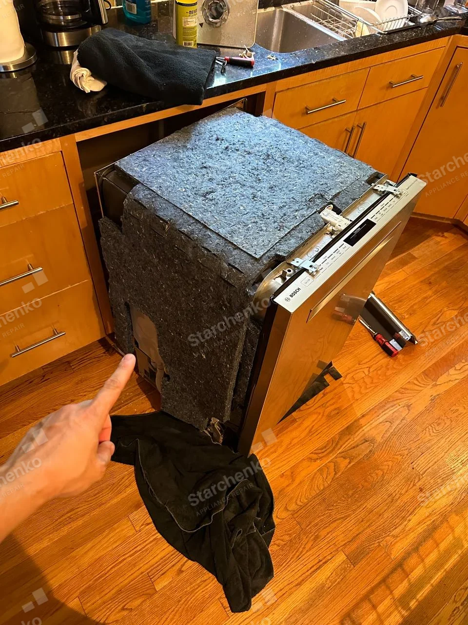 Bosch repair: Dishwasher pulled out from lower kitchen cabinetry with side sound blanket lifted and front door open.