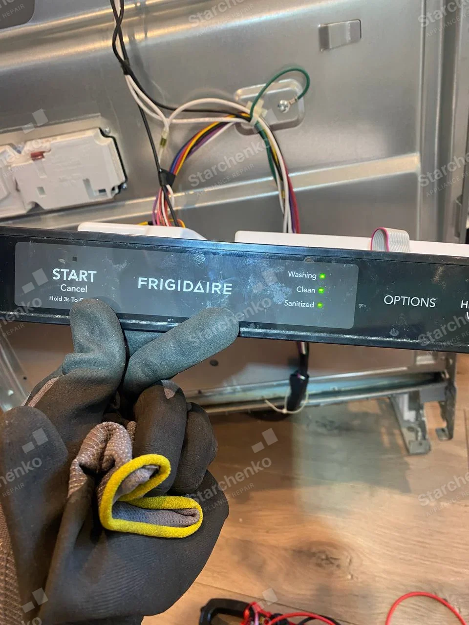 Frigidaire repair: Dishwasher control fascia removed with wires visible behind it, illuminated Washing, Clean, Sanitized indicators.