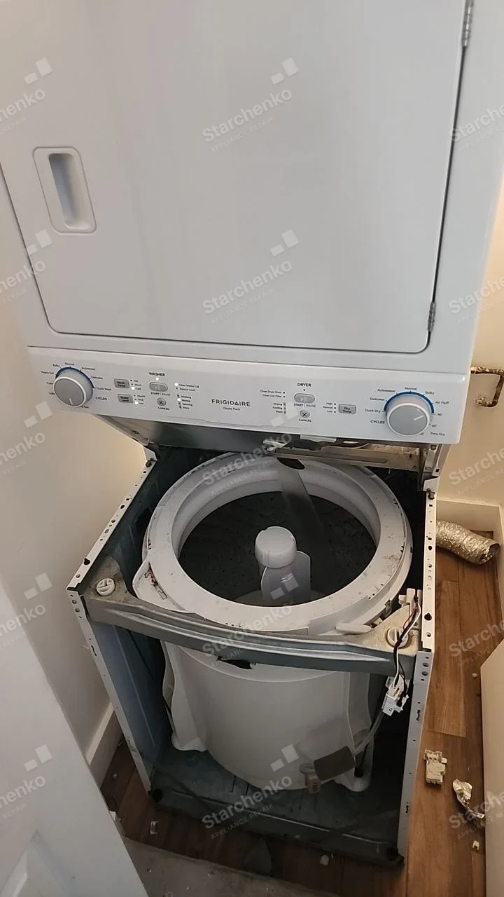 Frigidaire stacked laundry center with lower washer casing removed, exposing top-load tub beneath dryer.