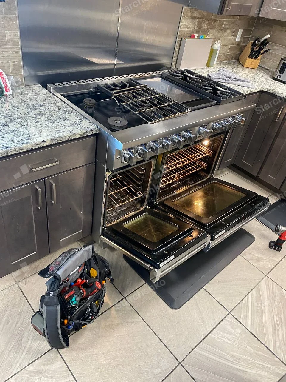 GE repair: Stainless gas range with two oven doors open and cooktop grates moved aside.