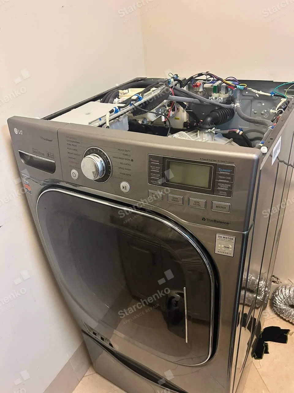 LG front-load washer with top cover removed exposing inlet hoses, tub and electronic controls.