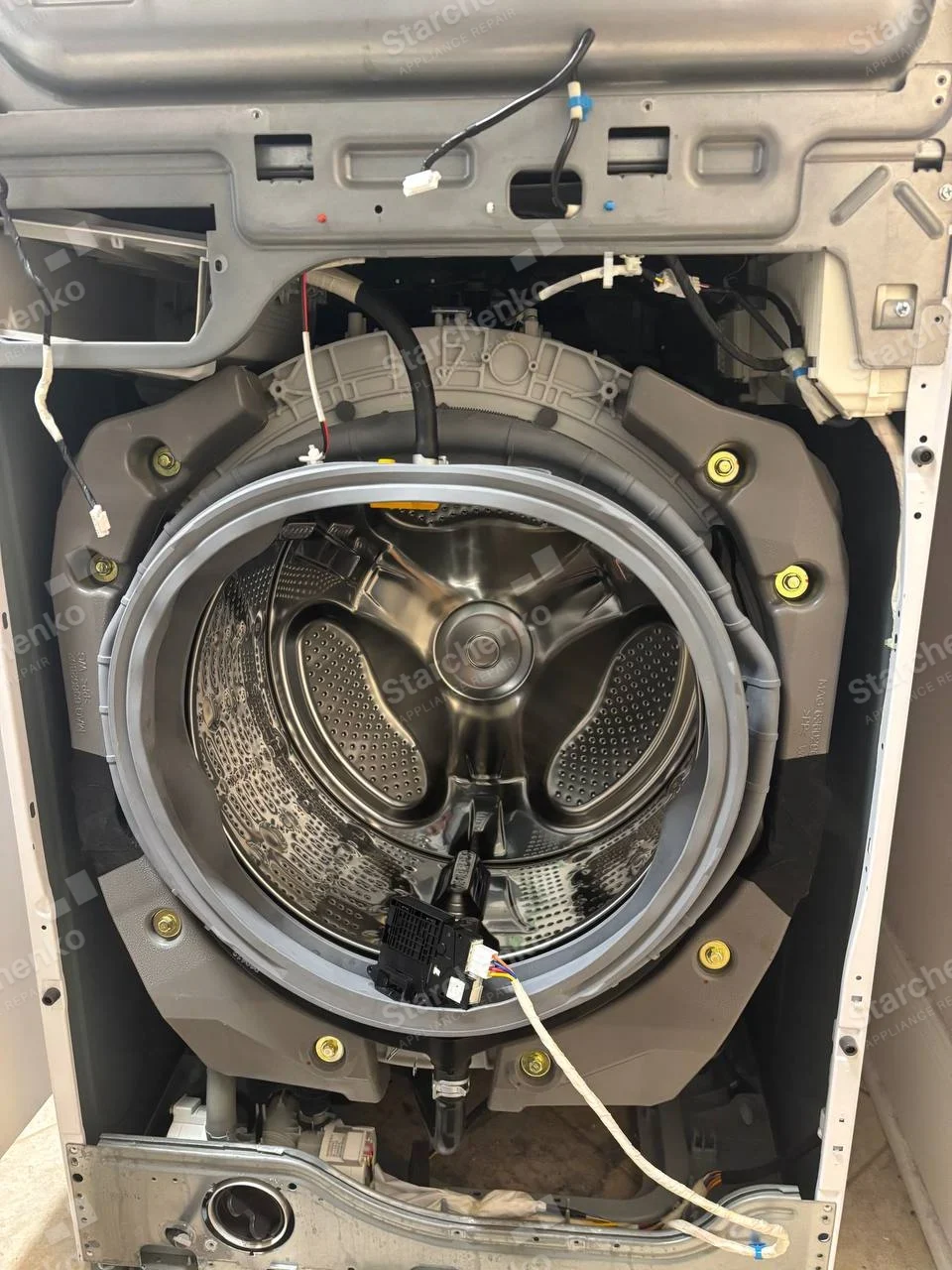 Frigidaire repair: Front-load washing-machine cabinet and door removed, showing drum, tub and door seal, no visible main brand.