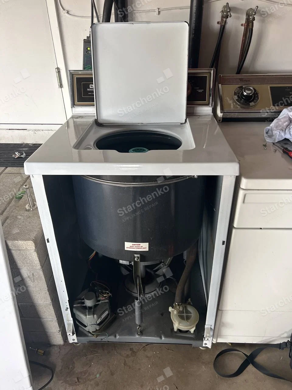 Maytag top-load washer with front cabinet removed, exposing tub, drive and pump.