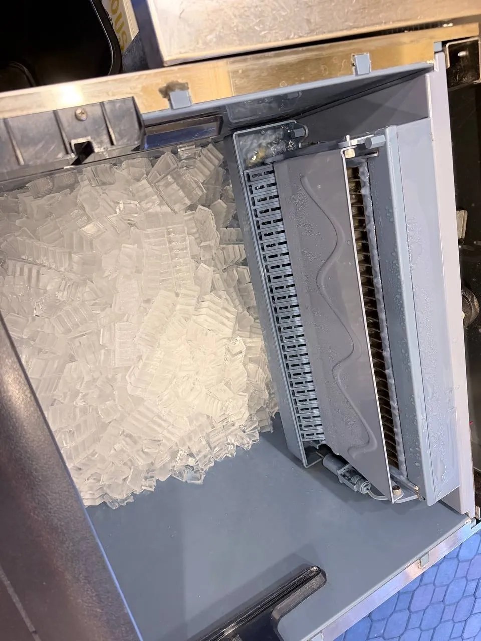 Ice maker opened with ice cubes spilled onto the floor