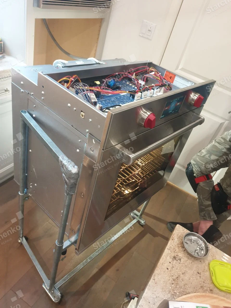 GE repair: Single wall oven pulled onto service cart, top control cover removed exposing boards and wires, lighted cavity.