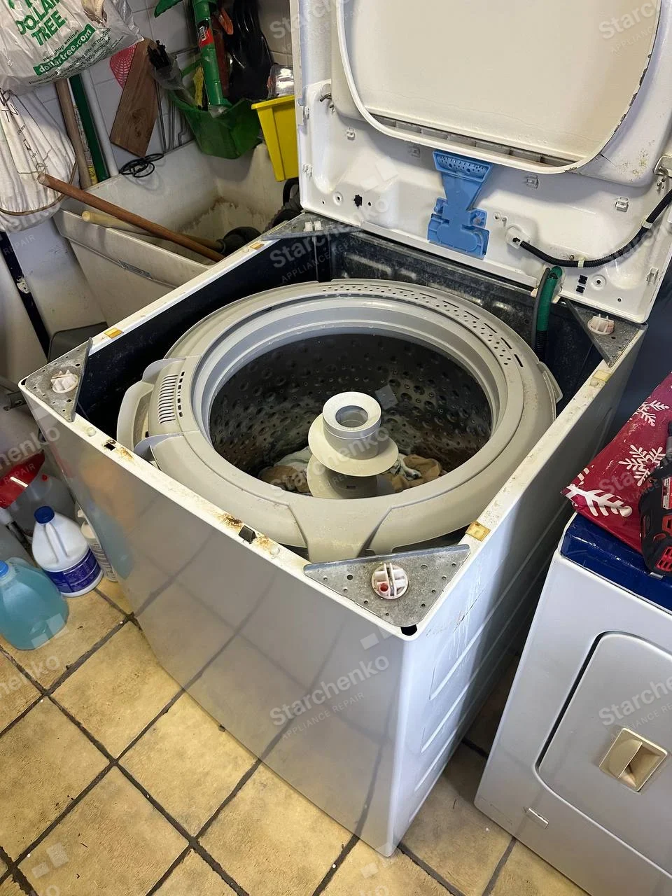Amana repair: Top-load washer lid raised and upper rim disassembled, revealing wash basket and central agitator.