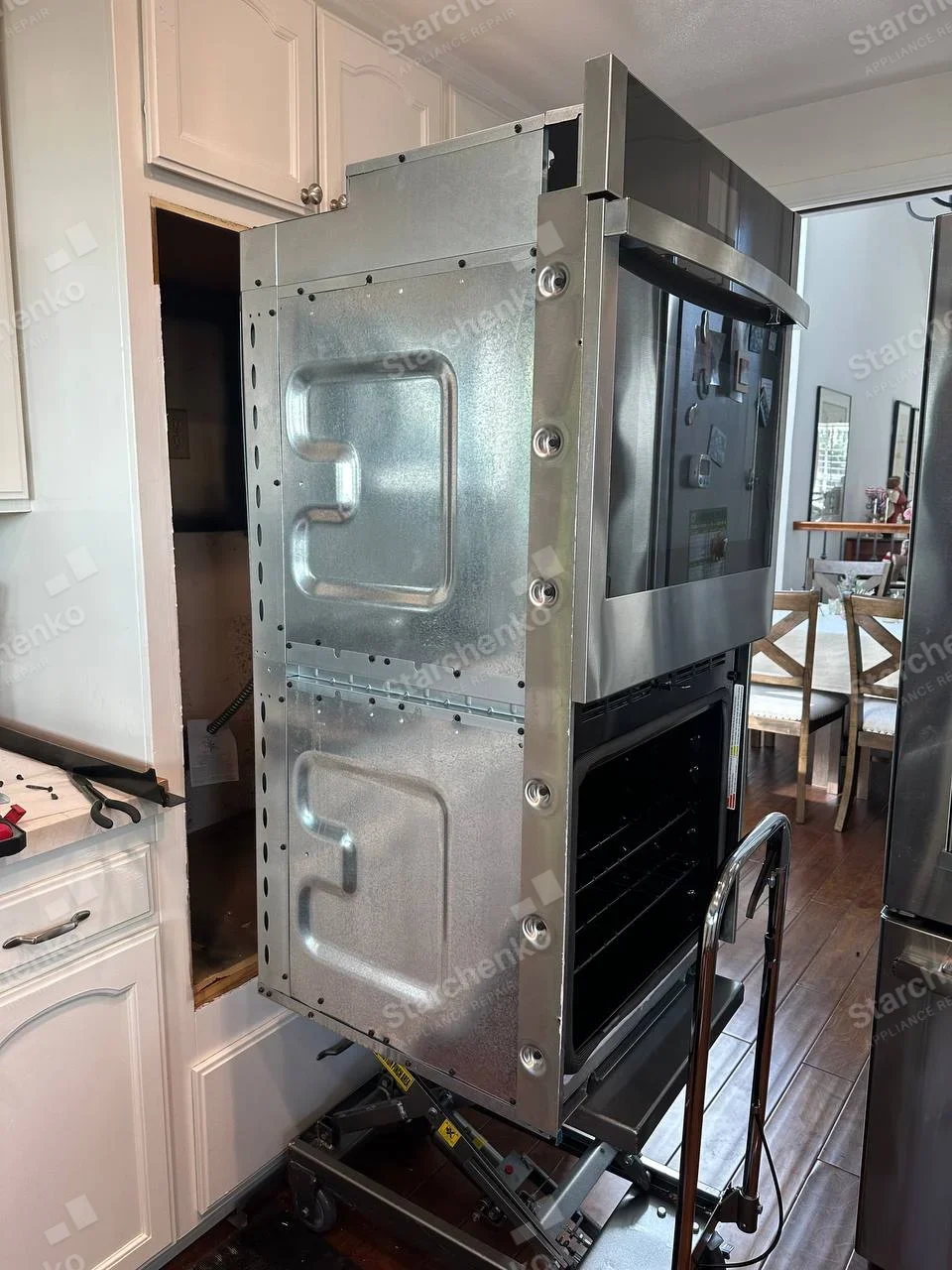 GE repair: Tall built-in cooking stack on service lift, upper microwave or compact oven and lower full-size oven, lower cavity open.