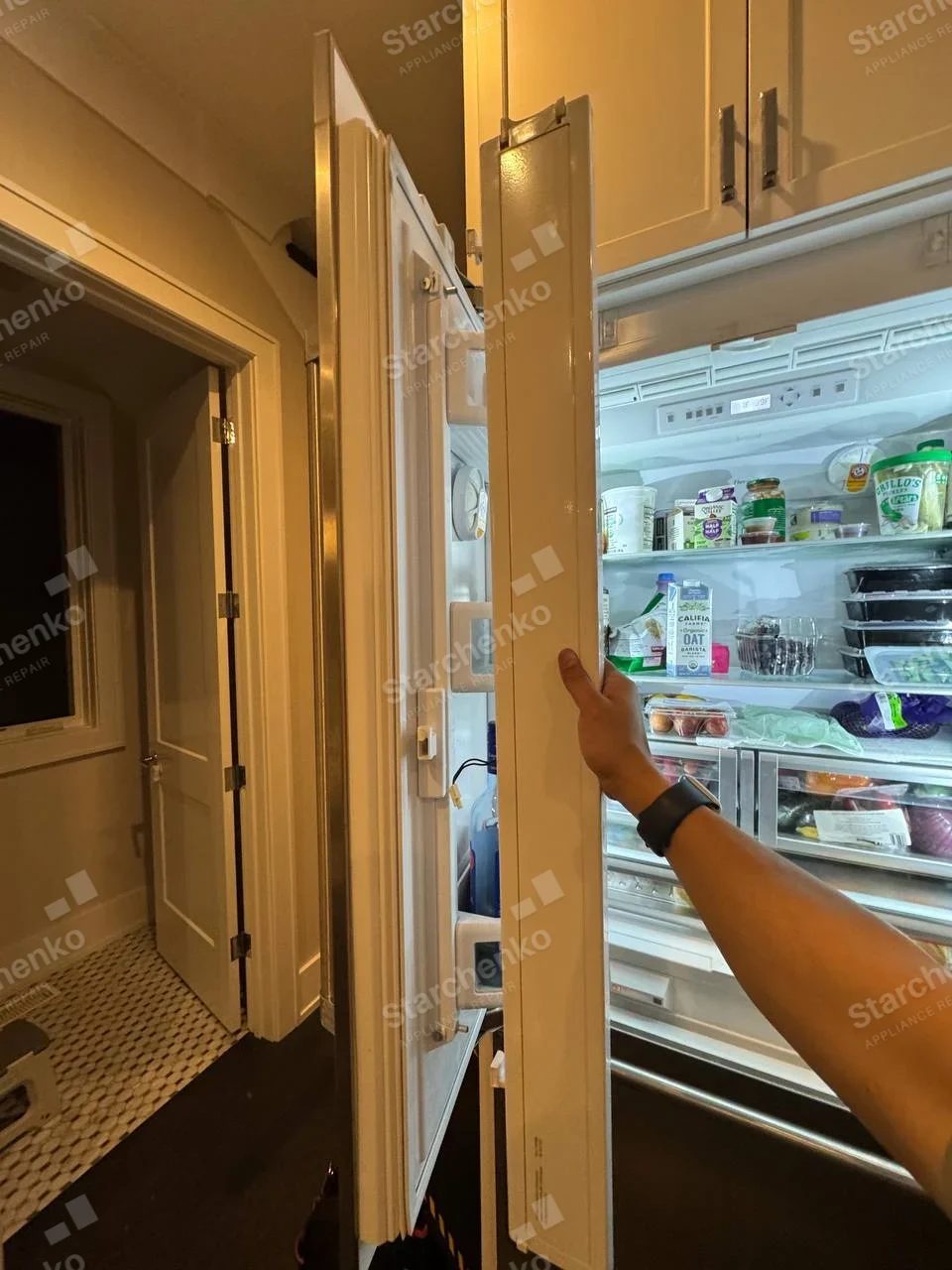 GE Profile repair: Open integrated refrigerator door and interior with technician holding decorative panel.