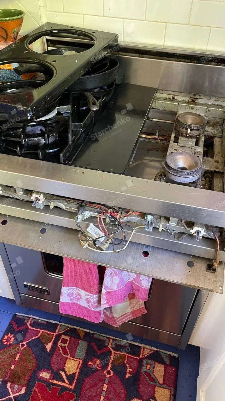 Viking badge at lower-left of oven door, cooktop and front control assembly removed exposing gas burner and wiring.