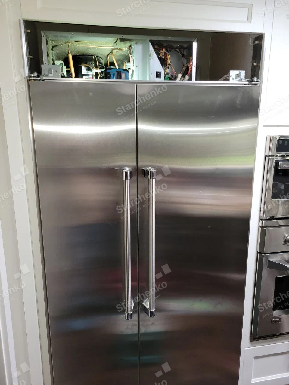 GE Profile repair: Stainless built-in side-by-side refrigerator with top grille removed and machinery exposed.