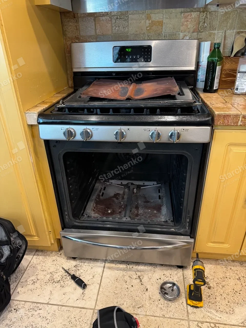 Frigidaire gas range with the oven door open and the oven floor panel removed to reach the burner